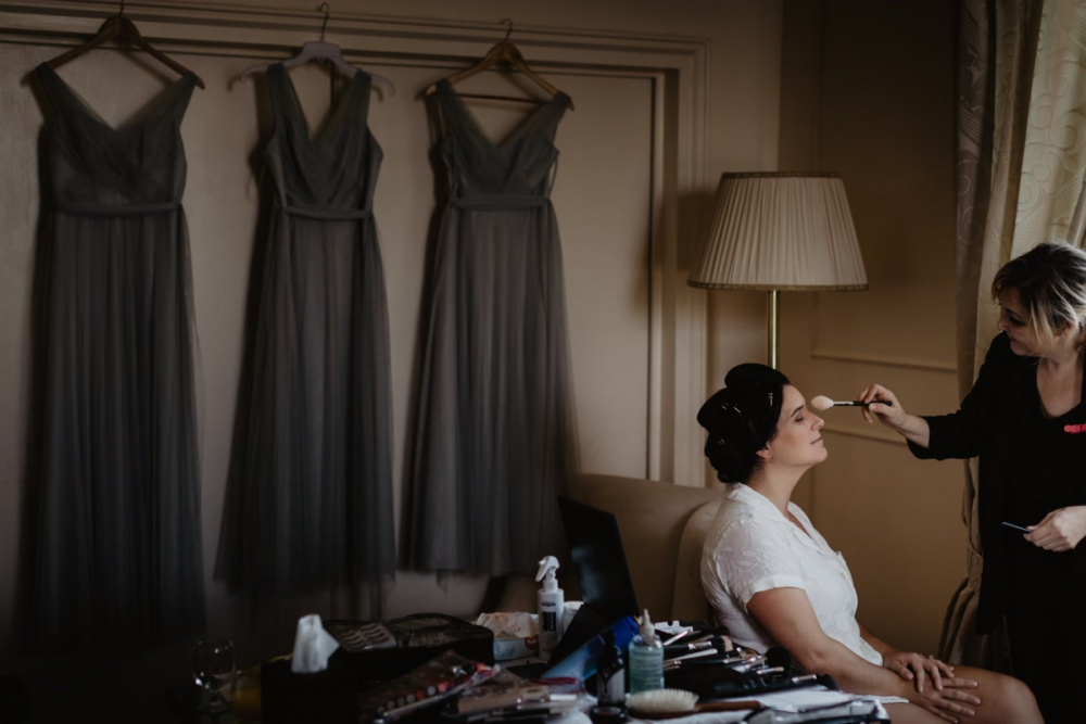 The bride is getting ready with the make up artist and three grey dress