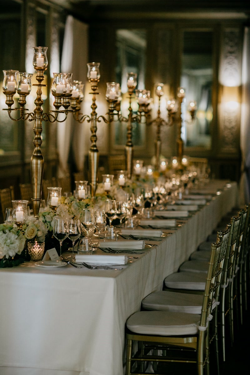 Table with gold candelabras, white table clothes, gold chairs and white and yellow flowers as wedding decor in Rome