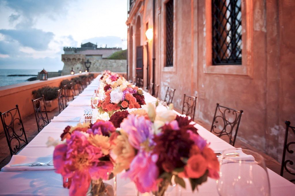 amazing long wedding table along the terrace over the sea with colourful fresh flowers at sunset